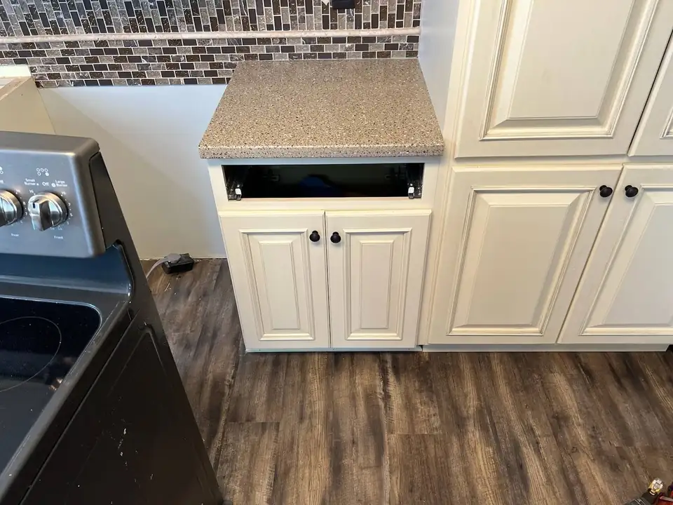 Countertops in East Moline: speckled tan solid surface top on cream raised-panel cabinets beside a mosaic tile backsplash, from M & L Countertops & More